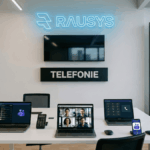 Modernes Büro-Setup mit Microsoft Teams Telefonie auf Laptop und Smartphone unter einem neonblauen "RAUSYS"-Logo
