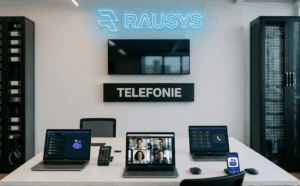 Modernes Büro-Setup mit Microsoft Teams Telefonie auf Laptop und Smartphone unter einem neonblauen "RAUSYS"-Logo